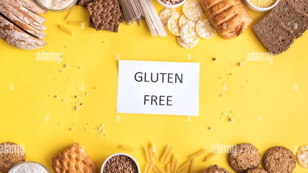 A selection of gluten-free foods, including quinoa, rice, fresh vegetables, fruits, and gluten-free bread, arranged on a kitchen counter.