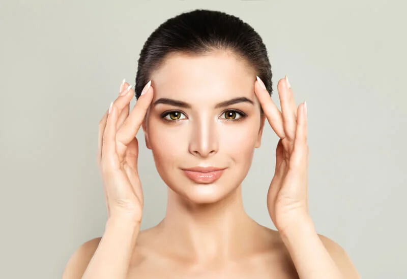 A close-up of a client's face with a creamy enzyme facial mask applied, while a skincare professional performs the treatment.