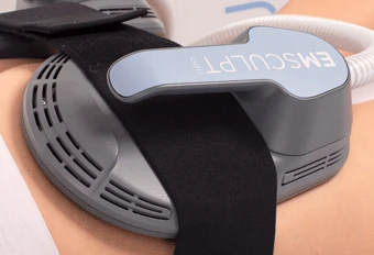 A person receiving an EMSCULPT treatment on their abdomen. The device is applied to the area, and the muscles are visibly contracting due to the electromagnetic energy.