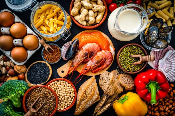 "Image of various common allergenic foods such as peanuts, milk, eggs, shellfish, and wheat on a wooden table, representing potential triggers for food allergies."