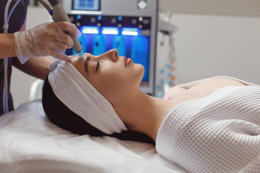 A close-up of a HydraFacial treatment, showing a professional using a specialized device to cleanse and hydrate a woman's skin.