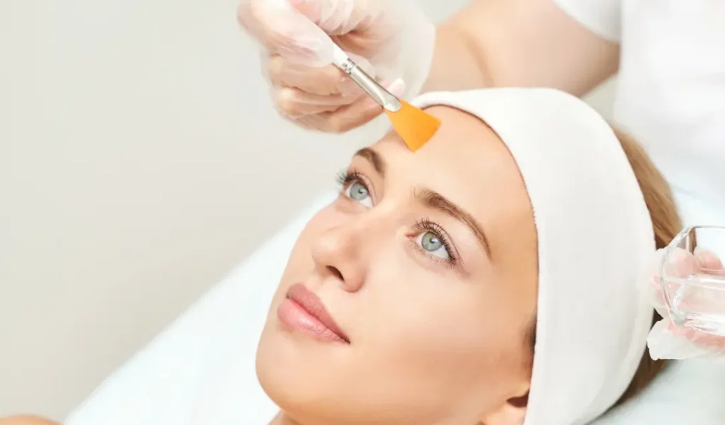 "Teenage girl receiving a chemical peel treatment in a modern clinic, with a professional applying a gentle solution to her face."